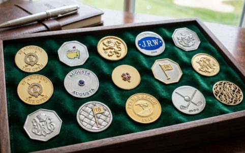 Collection of luxury golf ball markers in sterling silver and gold displayed on a green velvet surface