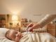 A mother checking her baby's temperature with a digital thermometer in a nursery.