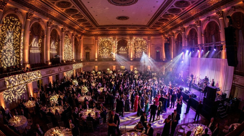 Elegant reception hall illuminated by vibrant purple up-lighting and crystal chandeliers.