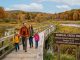 A family hiking a scenic boardwalk trail surrounded by autumn foliage and wetlands at a national wildlife refuge during National Wildlife Refuge Week 2026