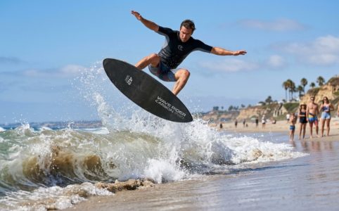 Fiberglass skimboard resting on wet sand with ocean waves at sunset.